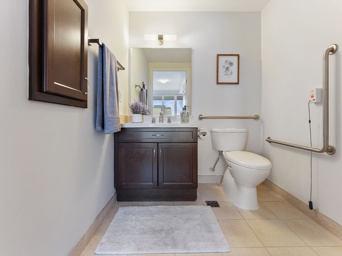 Bathroom at Walden Circle Retirement Home featuring a toilet, sink, and shower in a clean, accessible layout.